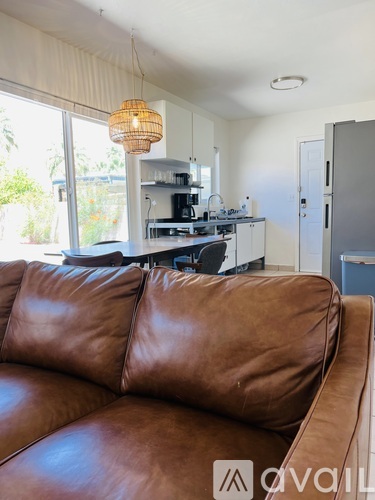 A brown leather couch in a living room with a kitchen in the background.