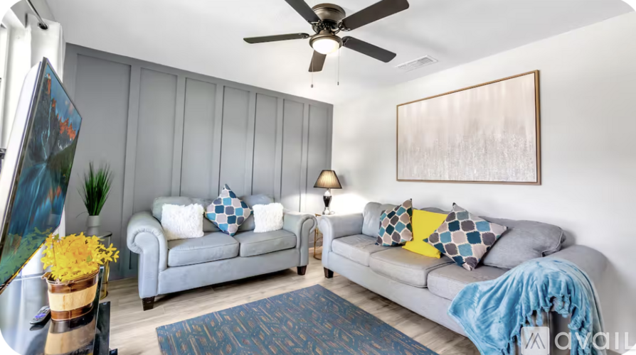 A living room with a grey couch, a blue blanket, and a painting on the wall.