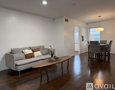 A living room with a grey couch, a wooden coffee table, and a dining table with chairs.
