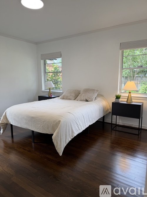 A bedroom with a white bed and wooden floors.