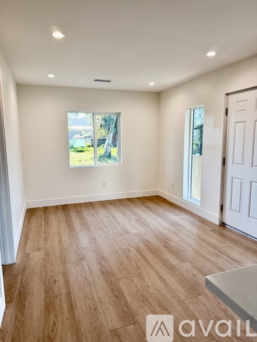 A room with wooden flooring and a window showing a view of trees and a building outside.