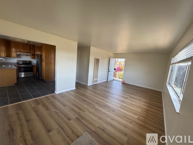 A spacious room with wooden flooring and a kitchen area in the background.