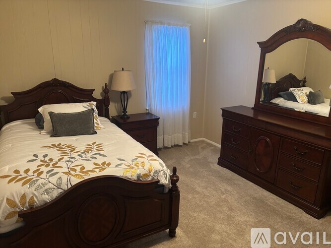 A bedroom with a large bed, a nightstand with a lamp, and a dresser with a mirror.