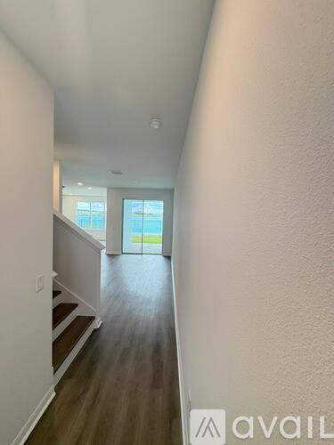 A hallway with wooden floors and white walls leading to a glass door.