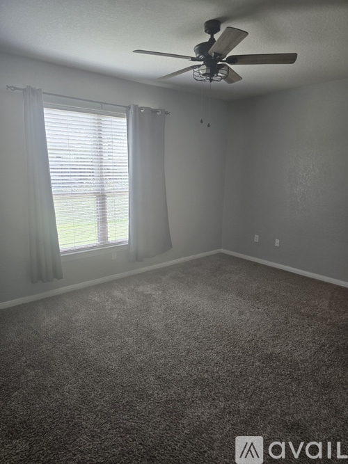 A room with a ceiling fan and a window with curtains.