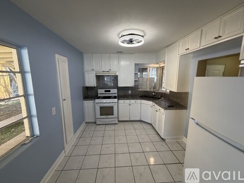 A kitchen with white cabinets and appliances, a window, and a tiled floor.