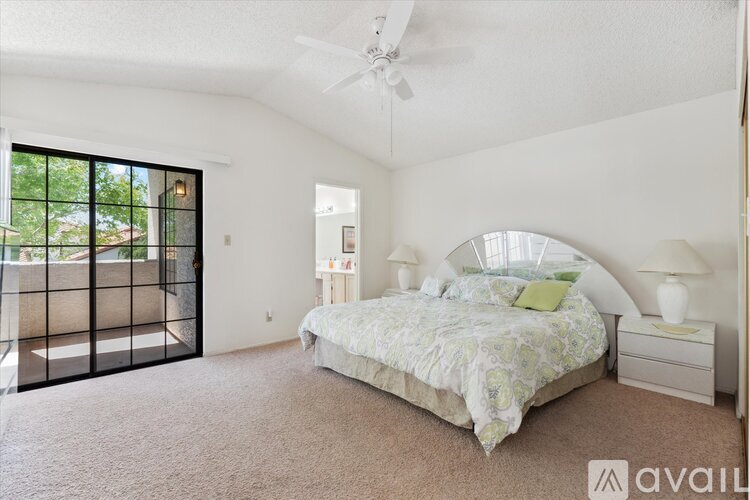A bedroom with a large bed, a ceiling fan, and a sliding glass door.