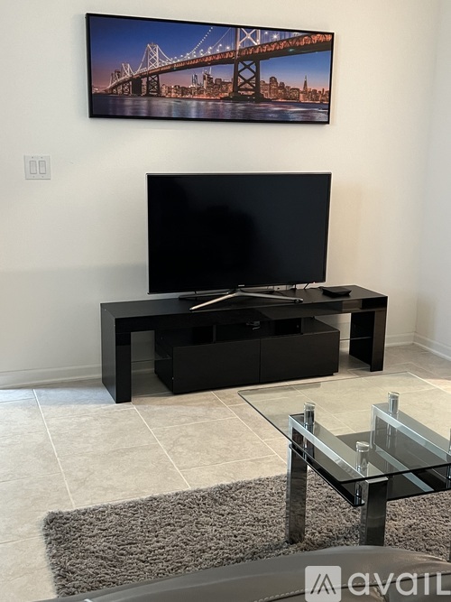 A black television set on a black stand with a glass table in front of it.