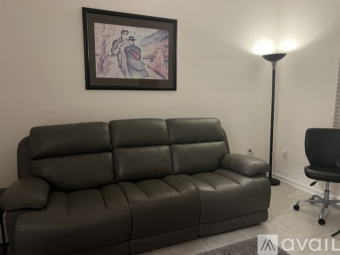 A black leather sofa in a room with a painting on the wall and a lamp.