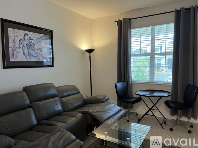 A black leather sofa sits in a living room with a glass table and a small round table with chairs.