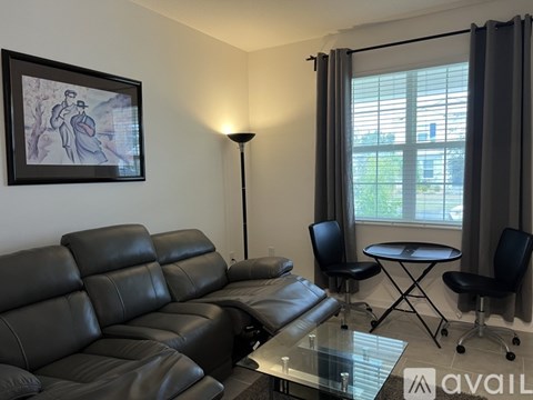 A black leather sofa sits in a living room with a glass table and a small round table with chairs.