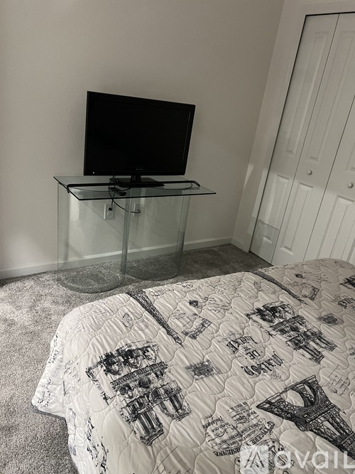 A bedroom with a bed, a glass table, and a television.