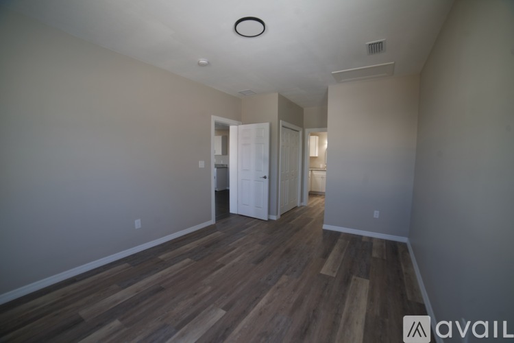 A room with wooden floors and white walls, with a doorway leading to another room.