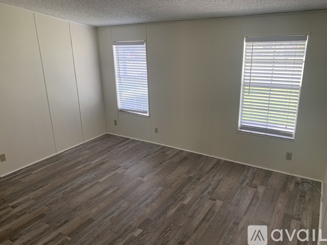 A room with wooden flooring and two windows with blinds.