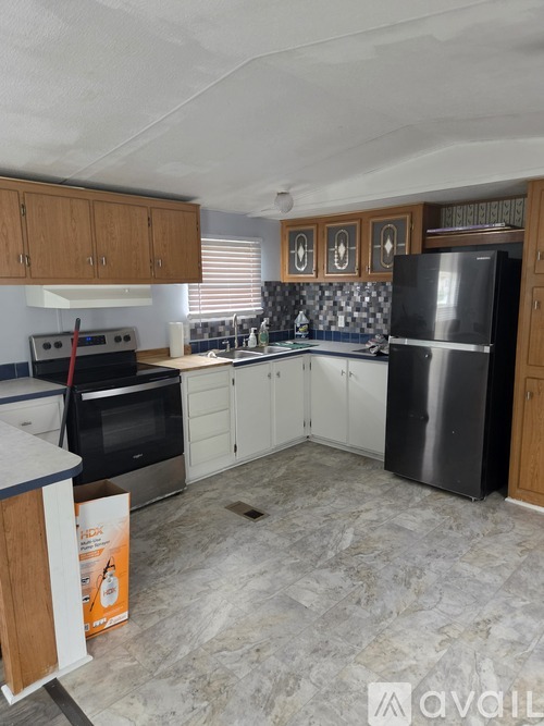 A kitchen with a black refrigerator, white countertops, and wooden cabinets.