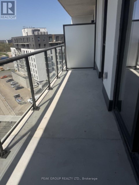 A balcony with a metal railing and a view of a parking lot and buildings.