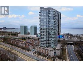 A modern glass building stands tall in the foreground of a cityscape with a body of water in the background.