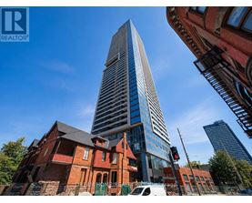 A tall, modern skyscraper stands in front of a red brick building.