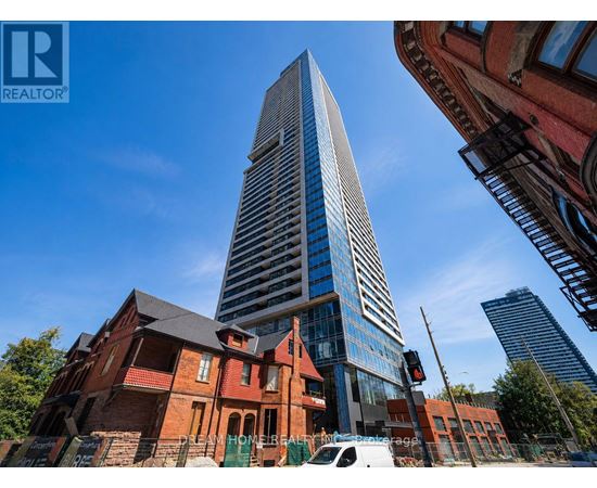 A tall, modern skyscraper stands in front of a red brick building.
