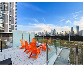A balcony with orange chairs and a table overlooking a city skyline.