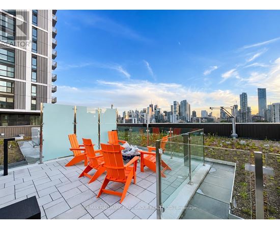 A balcony with orange chairs and a table overlooking a city skyline.