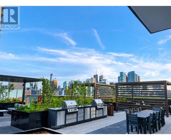 A rooftop patio with a grill and chairs overlooking a city skyline.