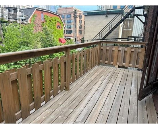 A wooden deck with a railing and a building with a red door in the background.