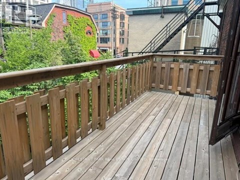 A wooden deck with a railing and a building with a red door in the background.