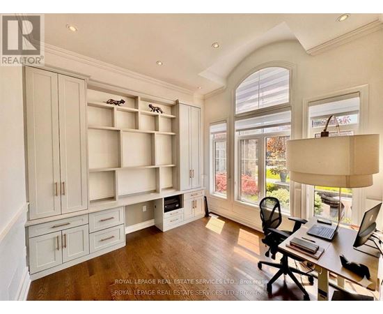 A well-lit room with a desk, chairs, and shelves.