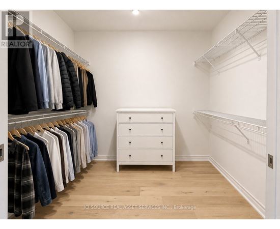 A white closet with clothes hanging and a white dresser.