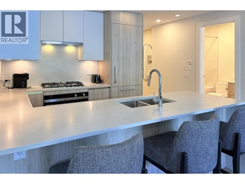 A modern kitchen with a large island and grey chairs.