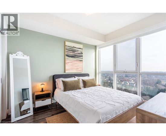 A bedroom with a large bed, a dresser, and a large window overlooking a cityscape.