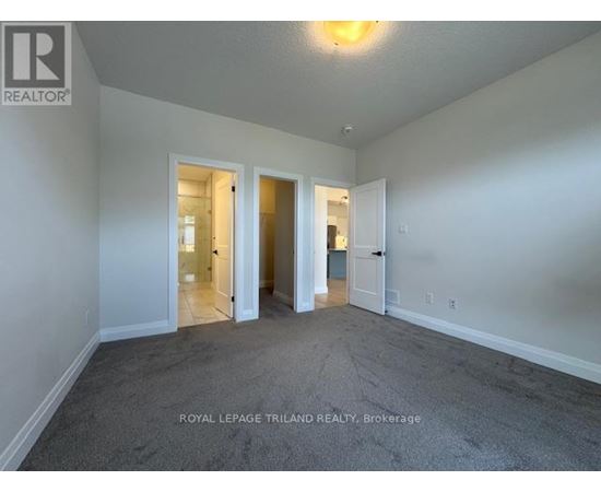 A spacious room with carpeted floor and white walls, with a doorway leading to another room.