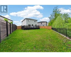 A grassy backyard with a fence and a house in the background.
