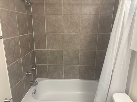 A bathroom with a white tub and grey tiles.