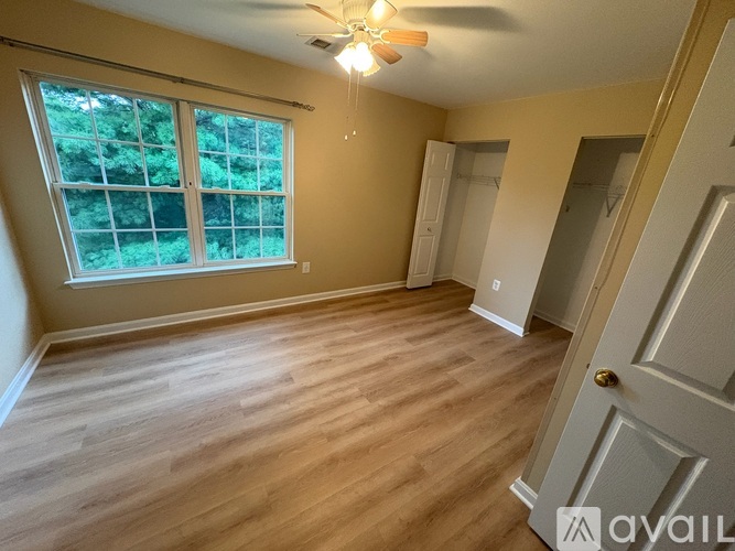 A room with wooden flooring and a window with a view of trees.