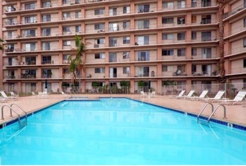 A large swimming pool in front of a multi-story apartment building.