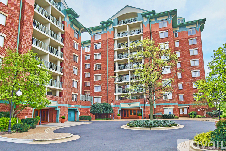A red brick apartment building with a green roof and a round driveway.