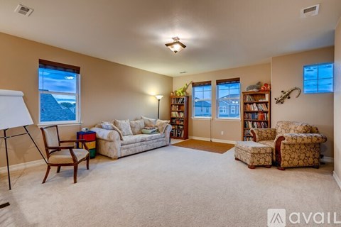 A living room with a large couch, a chair, a small ottoman, and a bookshelf filled with books.