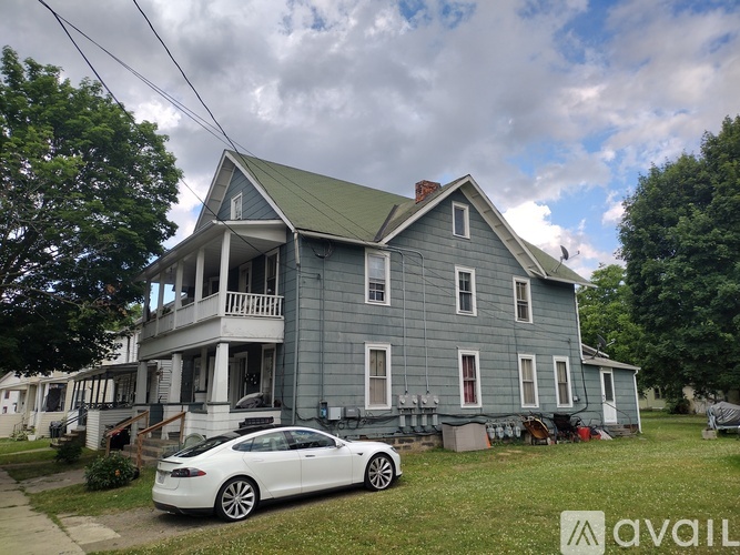 A white car is parked in front of a grey house.