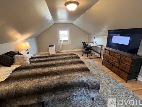 A bedroom with a bed covered in a grey furry blanket, a desk with a computer, and a television on a cabinet.