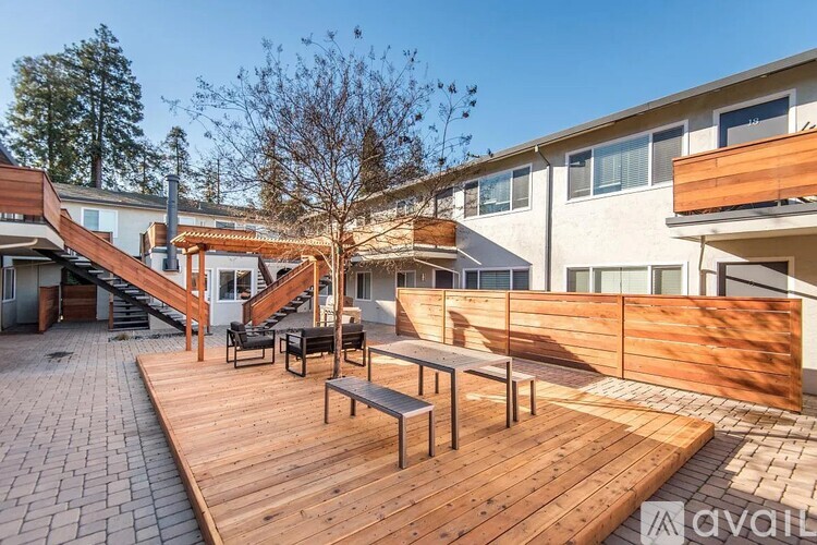 A wooden deck with benches and a tree in front of a white building.