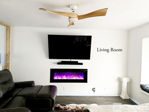 A living room with a black leather couch and a flat screen TV mounted above a fireplace.