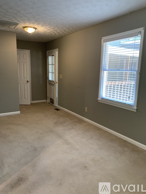 A room with a carpeted floor, a window with blinds, and a door.