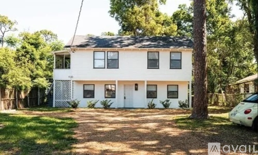 A white house with a black roof surrounded by greenery.