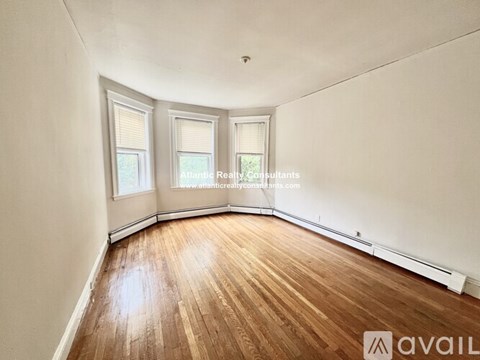 A room with wooden flooring and white walls, with two windows and a ceiling light.