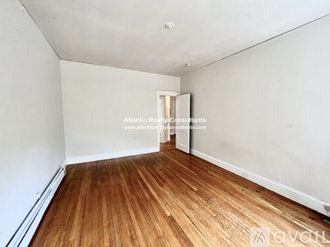 A room with wooden flooring and white walls, with a doorway leading to another room.
