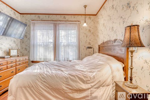 A bedroom with a bed, dresser, and window with curtains.