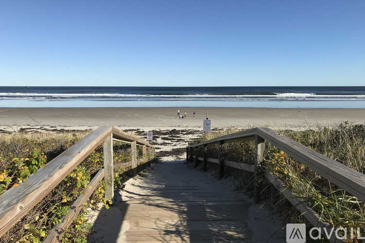 A wooden walkway leads to a beach with a clear blue sky above.