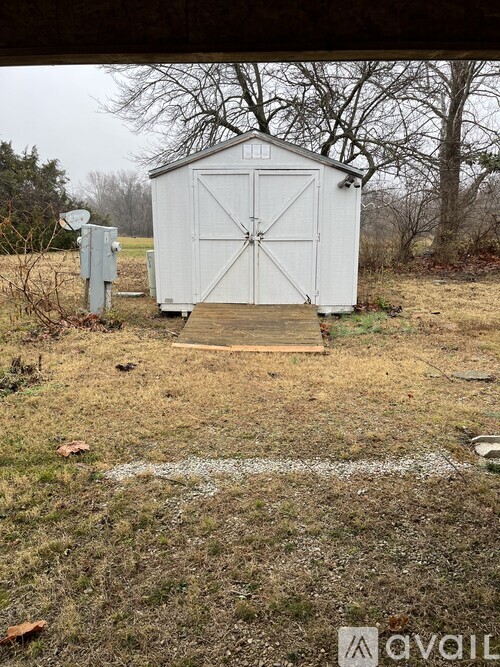 A small white shed with a wooden walkway leading to it.